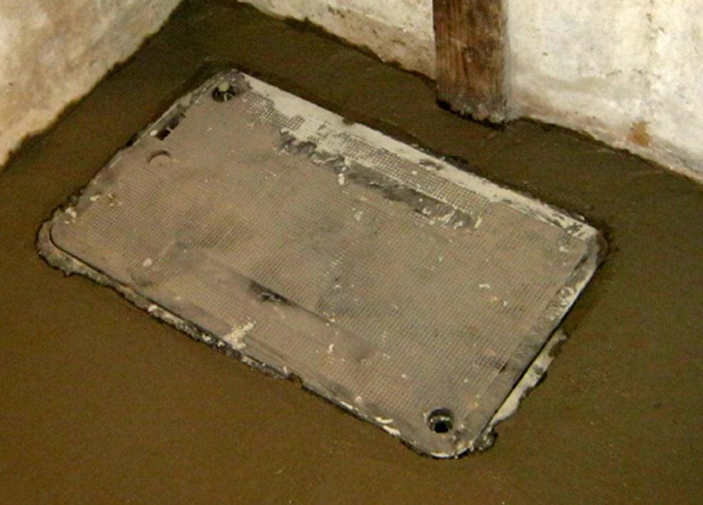 A sewer trap location is under the sewer access cover inside a basement