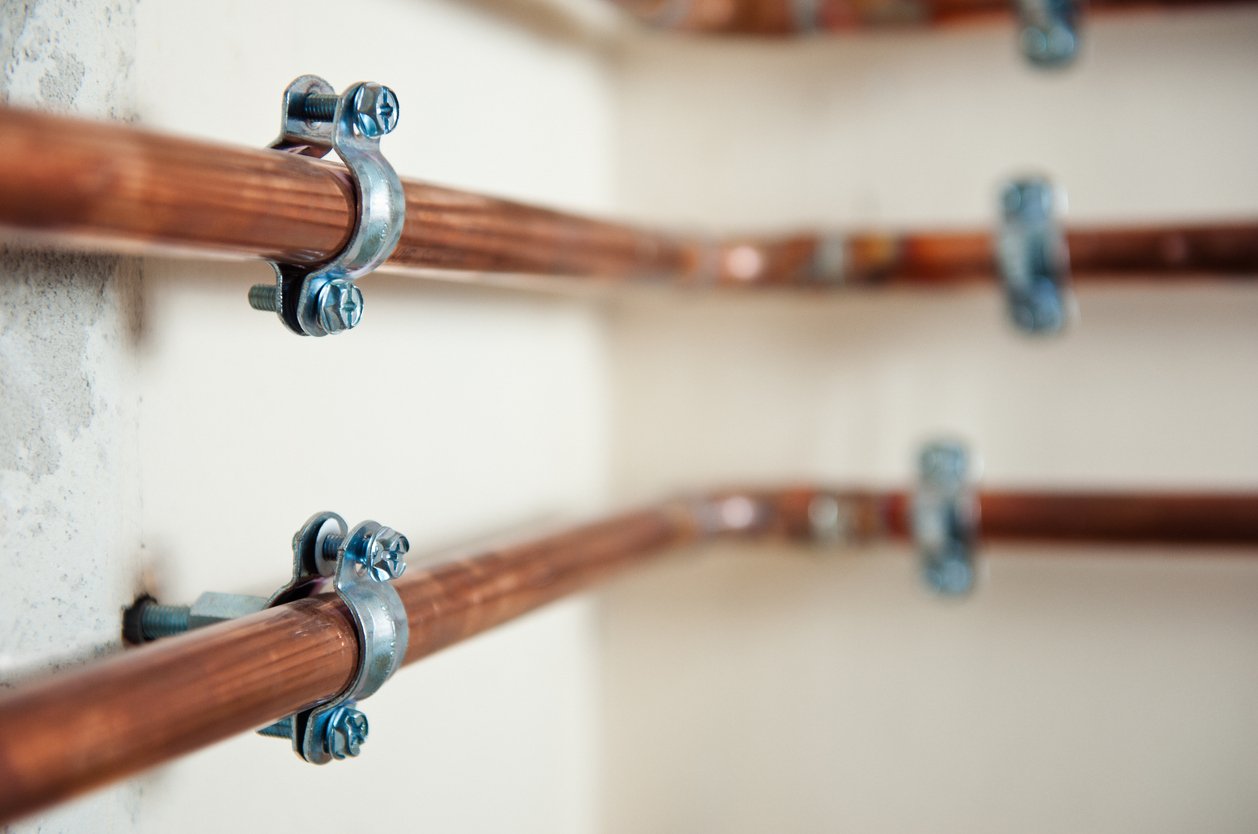 Copper pipes fastened on a wall by copper pipe clamps.