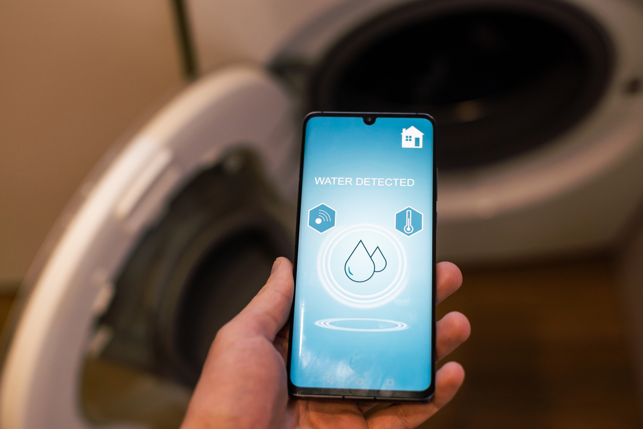 Man holding a smartphone showing a notification from his home's water alarm sensor.