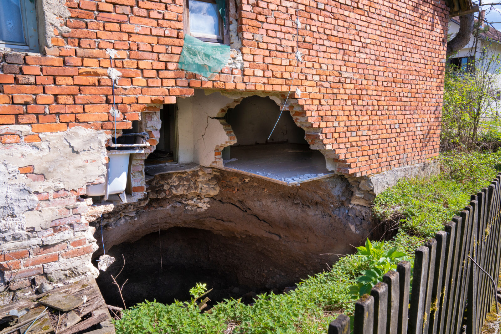 Sinkhole in a grass yard collapses a portion of a building