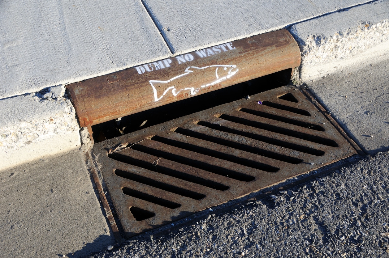 How Do Storm Drains Work? 3 Commercial property's storm drain with installed storm drain traps showing a sign prohibiting the dumping of waste.
